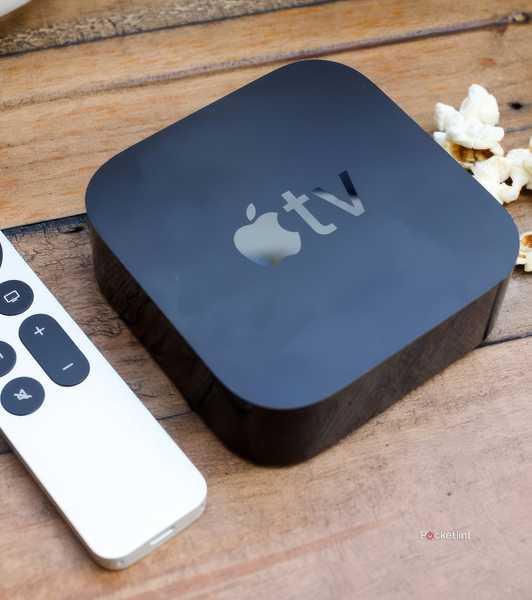 An Apple TV remote and box sit on a wood table next to popcorn.