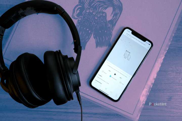 A pair of Audio-Technica headphones beside a phone streaming a song from Bandcamp, on top of a record