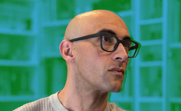 A person wearing black Halo smart glasses in front of a bookcase that's been edited to be blue and green.