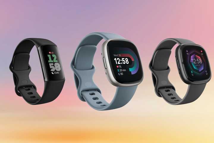 Three Fitbit watches are placed against a pastel sunset. 
