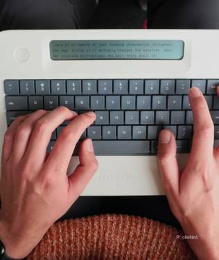 Two hands typing on a Freewrite Alpha on a lap.
