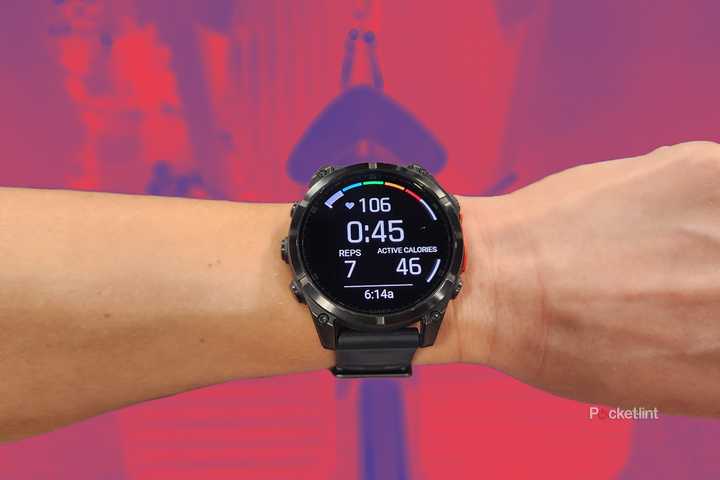 A wrist with the Garmin Fenix 8 watch is on a wrist that's held over a seated row machine that is tinted red and purple. 