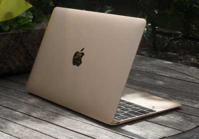 A gold 12-inch MacBook outside on a wooden table.
