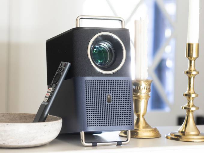 TCL A1 projector on a ledge with the remote and candlesticks