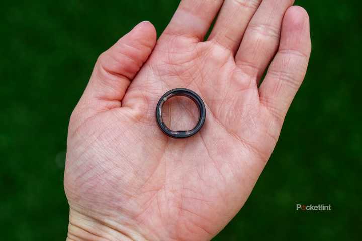 The Ultrahuman Ring Air sits on an open palm above a blurred green background. 