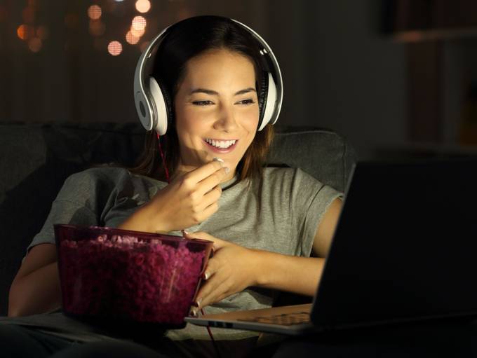 Woman watching movie on laptop with popcorn and headphones